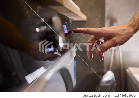 Individual Interacting with a Modern Washing Machines Control Panel for Efficient Laundry Tasks 134649666