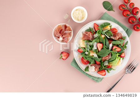 Fresh arugula salad with prosciutto, strawberries, cherry tomatoes, melon, parmesan. Healthy summer lunch concept. 134649819
