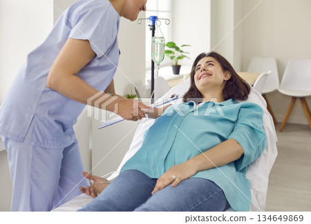 Nurse help pregnant woman in receiving IV drip infusion and vitamin therapy in medical clinic. 134649869