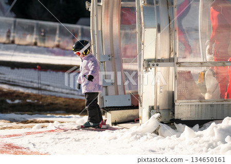 A girl on skis stands on a carpet ski lift in a glass tunel 134650161