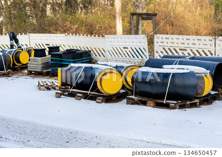 Insulated heating pipeline valves pallets urban site during winter energy maintenance utility. District heating equipment shows steel pipes, safety control technology public utility supply Germany 134650457
