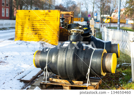 Insulated heating pipeline valves pallets urban site during winter energy maintenance utility. District heating equipment shows steel pipes, safety control technology public utility supply Germany 134650460
