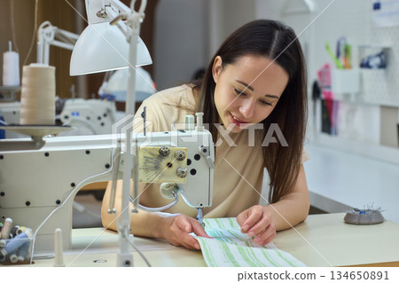 A Focused Seamstress Diligently Working with a Sewing Machine in Her Creative Workspace A Focused Seamstress Diligently Working with a Sewing Machine in Her Creative Workspace 134650891