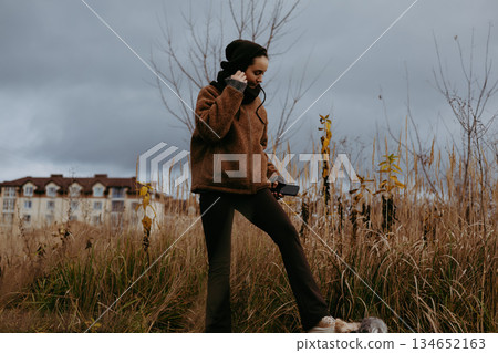 A modern girl in warm outerwear outdoors on a cloudy day. A woman is wearing a brown teddy jacket and hood on a cool day, walking outdoors alone. 134652163