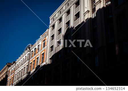 Dramatic urban contrast. Bright sunlight and deep shadow on modern and classic building facades with blue sky, symbolizing city life and modern architecture. A city street perspective view Real estate 134652314