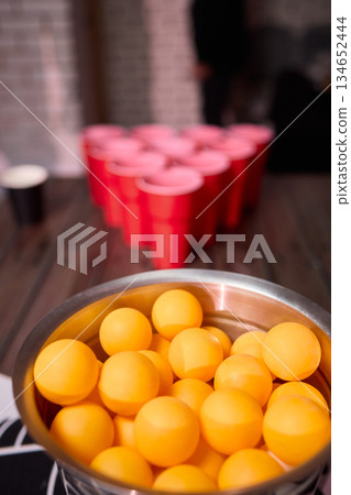 Party game setup, Playful indoor scene featuring ping pong balls and social accessories, Warmly lit indoor environment with beer pong essentials and lively social atmosphere 134652444