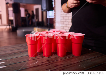 Party game setup, Playful indoor scene featuring ping pong balls and social accessories, Warmly lit indoor environment with beer pong essentials and lively social atmosphere 134652446