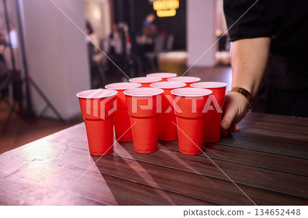 Party game setup, Playful indoor scene featuring ping pong balls and social accessories, Warmly lit indoor environment with beer pong essentials and lively social atmosphere 134652448