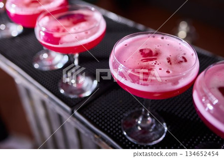 Mood setting with lively drink preparation at upscale bar, Elegant scene of bartender pouring colorful cocktail amidst festive warm lighting and guests in background 134652454