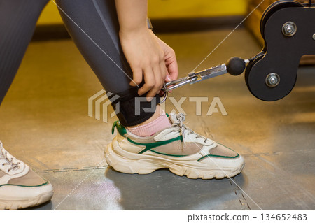 Closeup of athlete adjusting gear, Focusing on athlete readying for leg workout activity, Athlete carefully securing ankle strap on rubber floor environment before exercising Closeup of athlete adjusting gear, Focusing on athlete readying for leg workout activity, Athlete carefully securing ankle strap on rubber floor environment before exercising 134652483