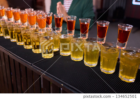 Celebratory drink scene, Orange liqueur shots at bar, Bartender pours drinks amidst lively party ambiance, Glassware reflects warm light during festive celebration at bar Celebratory drink scene, Orange liqueur shots at bar, Bartender pours drinks amidst lively party ambiance, Glassware reflects warm light during festive celebration at bar 134652501