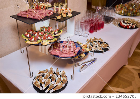 Elegant dining presentation, Sophisticated arrangement of canapes on stylish table setting, Exquisite black trays with gourmet delicacies showcased in upscale event ambiance 134652703