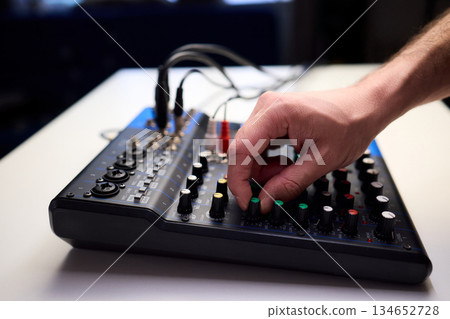 Tactile fingers manipulate illuminated dials during soundcheck setup, Professional technician finetunes sound equipment with multiple cables connected under moody studio lighting 134652728