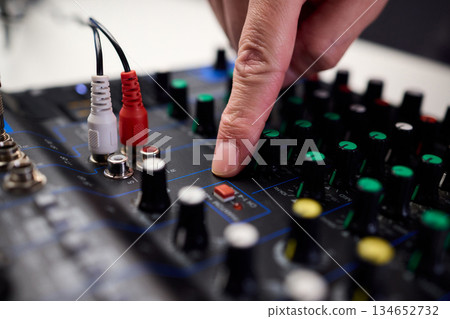 Tactile fingers manipulate illuminated dials during soundcheck setup, Professional technician finetunes sound equipment with multiple cables connected under moody studio lighting 134652732