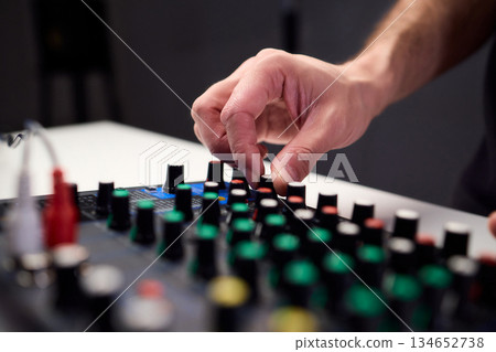 Closeup of hands adjusting mixer with glowing LED indicators and cables, Detailed image of operator controlling mixer dials and monitoring sound through sensors and LEDs Closeup of hands adjusting mixer with glowing LED indicators and cables, Detailed image of operator controlling mixer dials and monitoring sound through sensors and LEDs 134652738