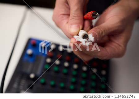 Personnel meticulously maintain audio equipment hygiene, Detailed shot of technician carefully cleaning audio cable with soft cloth in professional studio environment 134652742