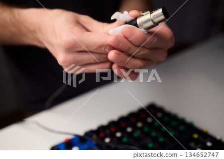 Personnel meticulously maintain audio equipment hygiene, Detailed shot of technician carefully cleaning audio cable with soft cloth in professional studio environment Personnel meticulously maintain audio equipment hygiene, Detailed shot of technician carefully cleaning audio cable with soft cloth in professional studio environment 134652747