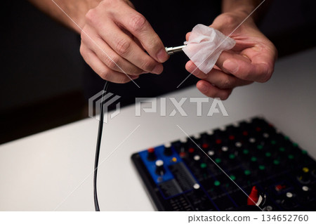 Personnel meticulously maintain audio equipment hygiene, Detailed shot of technician carefully cleaning audio cable with soft cloth in professional studio environment 134652760