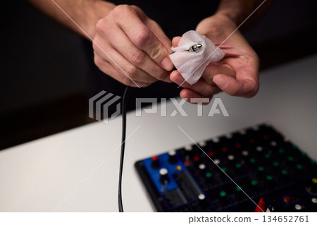 Personnel meticulously maintain audio equipment hygiene, Detailed shot of technician carefully cleaning audio cable with soft cloth in professional studio environment 134652761