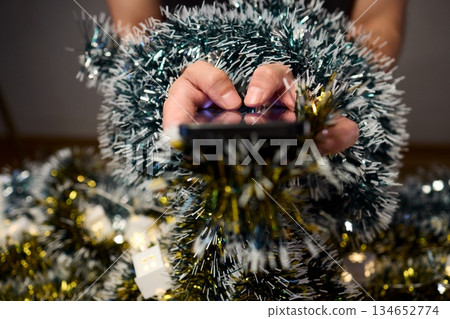 Digital holiday planning, Person reviewing online presents on tabletop, Warm indoor scene of individual managing digital gift list amidst festive lights and ornaments Digital holiday planning, Person reviewing online presents on tabletop, Warm indoor scene of individual managing digital gift list amidst festive lights and ornaments 134652774