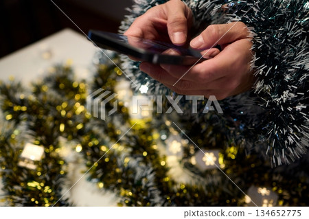 Digital holiday planning, Person reviewing online presents on tabletop, Warm indoor scene of individual managing digital gift list amidst festive lights and ornaments Digital holiday planning, Person reviewing online presents on tabletop, Warm indoor scene of individual managing digital gift list amidst festive lights and ornaments 134652775