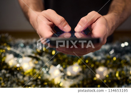 Digital holiday planning, Person reviewing online presents on tabletop, Warm indoor scene of individual managing digital gift list amidst festive lights and ornaments Digital holiday planning, Person reviewing online presents on tabletop, Warm indoor scene of individual managing digital gift list amidst festive lights and ornaments 134653195
