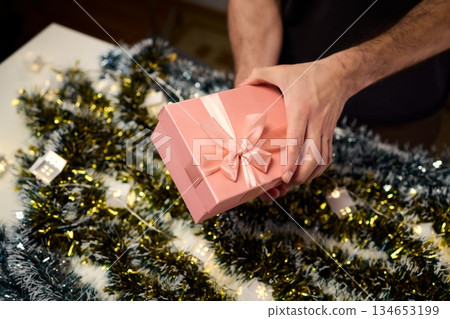 Carefully wrapped present with shimmering ribbons enhances holiday atmosphere, An intimate scene of gift gifting capturing warmth of festive seasonal preparations Carefully wrapped present with shimmering ribbons enhances holiday atmosphere, An intimate scene of gift gifting capturing warmth of festive seasonal preparations 134653199