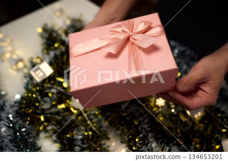Carefully wrapped present with shimmering ribbons enhances holiday atmosphere, An intimate scene of gift gifting capturing warmth of festive seasonal preparations Carefully wrapped present with shimmering ribbons enhances holiday atmosphere, An intimate scene of gift gifting capturing warmth of festive seasonal preparations 134653201