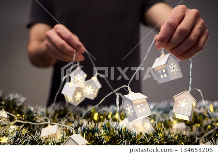 Decorative festive scene, Intimate shot of illuminated cottages with festive accents, Careful arrangement of tiny fairy lights over pine garland and glowing cottages 134653206