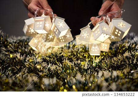 Decorative festive scene, Intimate shot of illuminated cottages with festive accents, Careful arrangement of tiny fairy lights over pine garland and glowing cottages Decorative festive scene, Intimate shot of illuminated cottages with festive accents, Careful arrangement of tiny fairy lights over pine garland and glowing cottages 134653222
