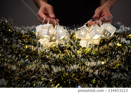 Decorative festive scene, Intimate shot of illuminated cottages with festive accents, Careful arrangement of tiny fairy lights over pine garland and glowing cottages Decorative festive scene, Intimate shot of illuminated cottages with festive accents, Careful arrangement of tiny fairy lights over pine garland and glowing cottages 134653223