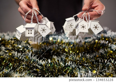 Decorative festive scene, Intimate shot of illuminated cottages with festive accents, Careful arrangement of tiny fairy lights over pine garland and glowing cottages 134653228