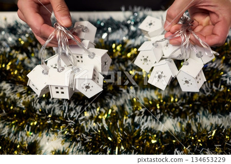 Decorative festive scene, Intimate shot of illuminated cottages with festive accents, Careful arrangement of tiny fairy lights over pine garland and glowing cottages 134653229