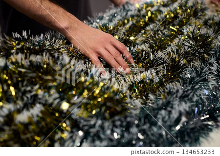 Closeup of hands preparing decorations, People arranging sparkling tinsel for celebration, Individuals meticulously position shimmering tinsel for seasonal festivity setup 134653233