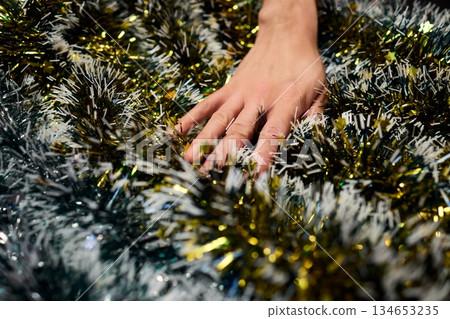Closeup of hands preparing decorations, People arranging sparkling tinsel for celebration, Individuals meticulously position shimmering tinsel for seasonal festivity setup 134653235