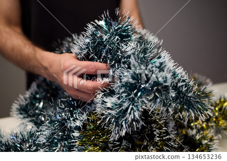 Closeup of hands preparing decorations, People arranging sparkling tinsel for celebration, Individuals meticulously position shimmering tinsel for seasonal festivity setup 134653236