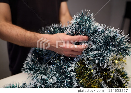 Closeup of hands preparing decorations, People arranging sparkling tinsel for celebration, Individuals meticulously position shimmering tinsel for seasonal festivity setup Closeup of hands preparing decorations, People arranging sparkling tinsel for celebration, Individuals meticulously position shimmering tinsel for seasonal festivity setup 134653237