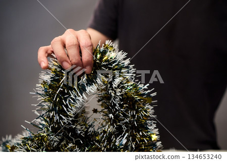 Closeup of hands preparing decorations, People arranging sparkling tinsel for celebration, Individuals meticulously position shimmering tinsel for seasonal festivity setup 134653240