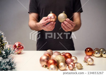 Hands arranging Christmas New Year baubles on white table with tinsel and warm bokeh lights, metallic red gold pink palette, careful styling by home decorator, festive craft mood Hands arranging Christmas New Year baubles on white table with tinsel and warm bokeh lights, metallic red gold pink palette, careful styling by home decorator, festive craft mood 134653267