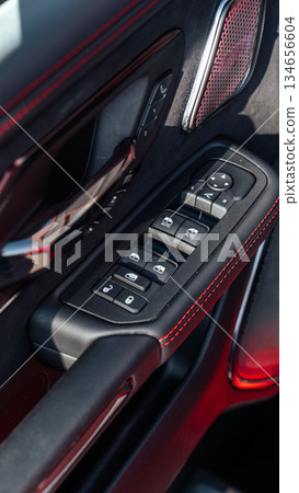 Car door control panel with modern design and vibrant red accents beside plush upholstery 134656604