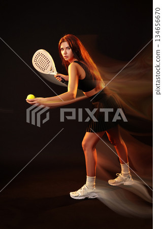 Tennis player preparing to serve a ball in a dramatic indoor setting 134656670