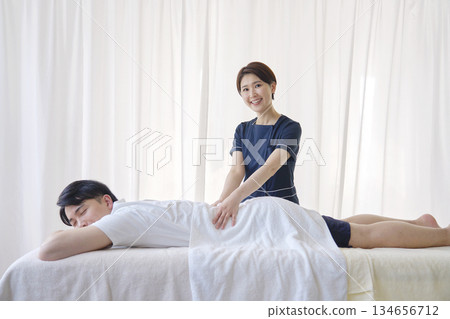 Portrait of a masseuse massaging a man's lower back Portrait of a masseuse massaging a man's lower back 134656712