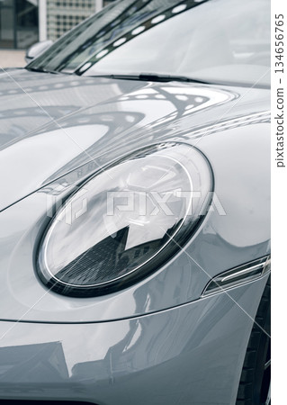 Close-up of a sleek car headlight by a modern building in urban setting 134656765
