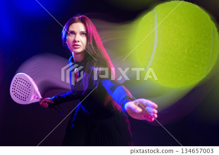 Woman playing tennis in dramatic lighting with a focus on a flying ball 134657003