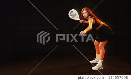 Young woman preparing to play racket sport in a dark indoor setting with dramatic lighting 134657008