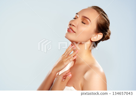 Woman applying cream to her skin while smiling and enjoying the moment in a studio setting 134657043