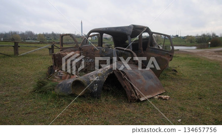 decrepit automobile skeleton surrounded by disorganized wreckage and natural overgrowth, decayridden vehicle structure with exposed components amidst field of fallen debris and muted lighting 134657756