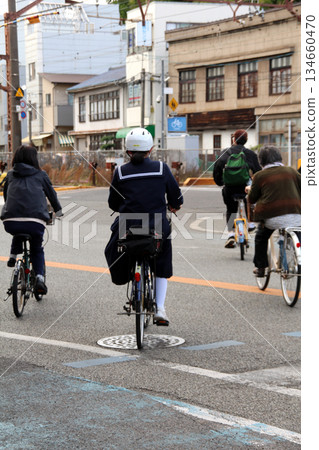 A high school girl wearing a helmet commuting to school by bicycle A high school girl wearing a helmet commuting to school by bicycle 134660470