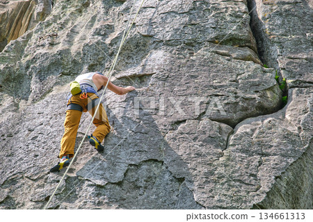 Strong male climber climbing steep wall of rocky mountain. Sportsman overcoming difficult route. Engaging in extreme sports hobby concept. Strong male climber climbing steep wall of rocky mountain. Sportsman overcoming difficult route. Engaging in extreme sports hobby concept. 134661313