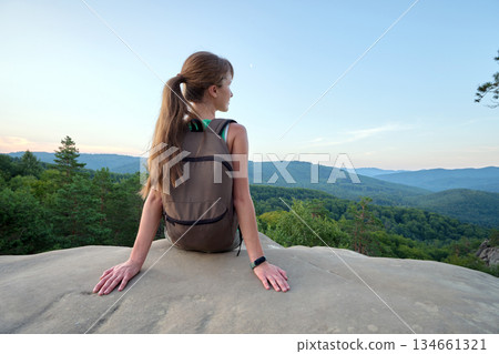 Sportive woman sitting alone taking a break on hillside trail. Female hiker enjoying view of nature from rocky cliff on wilderness path. Active lifestyle concept Sportive woman sitting alone taking a break on hillside trail. Female hiker enjoying view of nature from rocky cliff on wilderness path. Active lifestyle concept 134661321